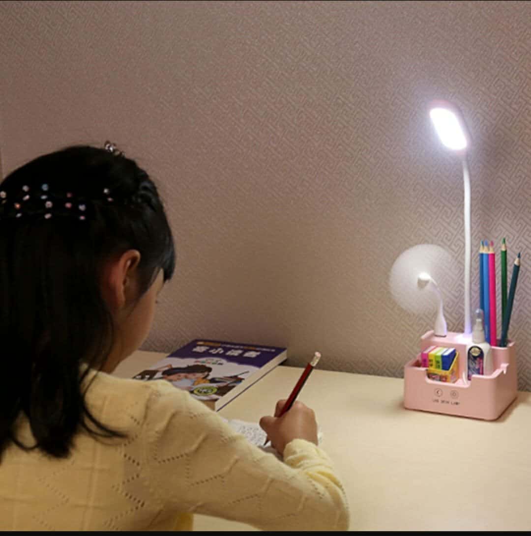 Cute girl studying with desk lamp and colorful stationery for kids educational activities.